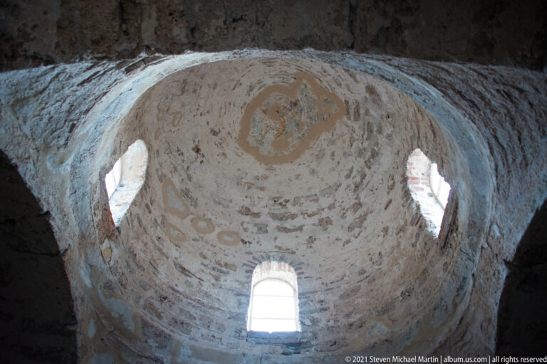 Upward view of a pale dome inside St. Sophia with narrow arched windows and faint decorative traces.
