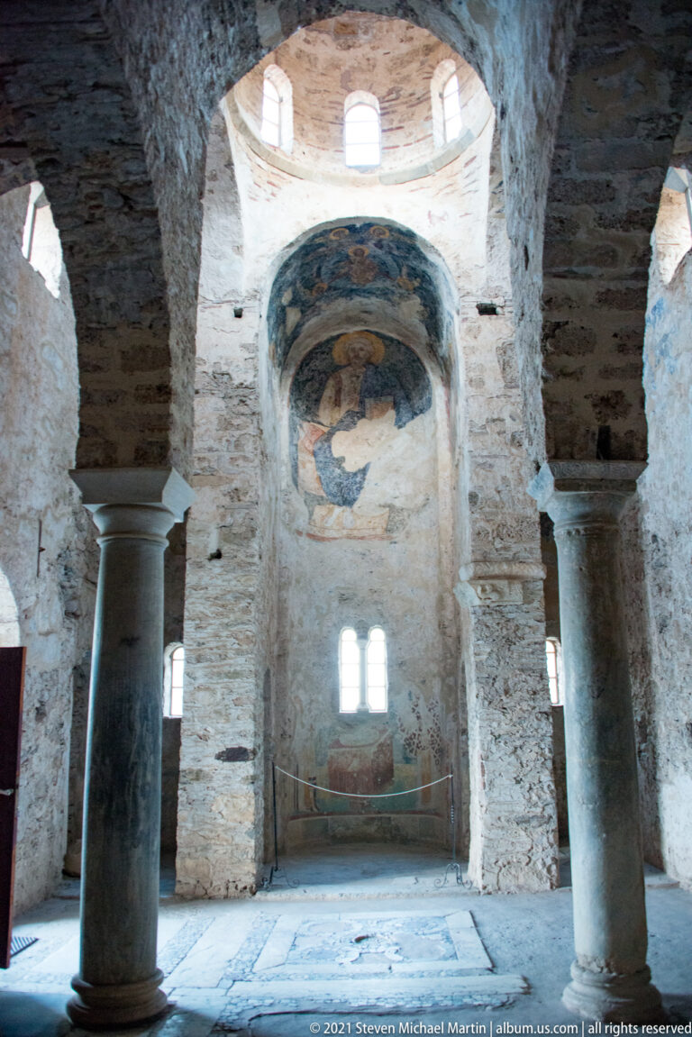 Wide interior of St. Sophia with stone columns, brick arches, high windows, dome, and a frescoed recess.