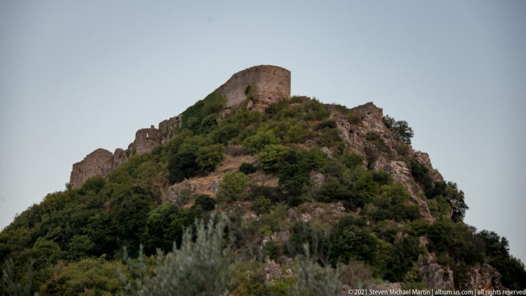 Upper fortifications of Mystras crowning a steep wooded hill, with massive walls and a prominent summit tower.