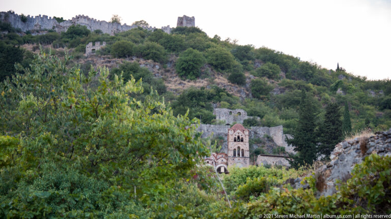 Pantanassa Monastery church appears among trees below the long stone walls of Mystras.