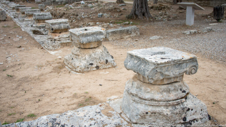 Aligned Ionic bases and carved supports from the outer colonnade of the Leonidaion at Ancient Olympia.