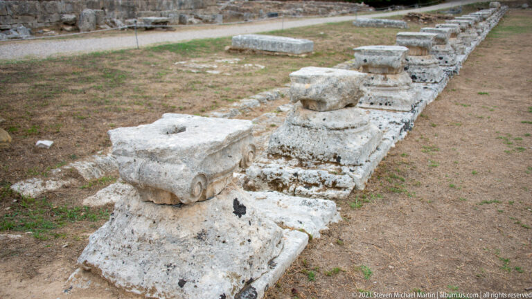 Long row of surviving column bases tracing the outer colonnade of the Leonidaion guesthouse at Olympia.