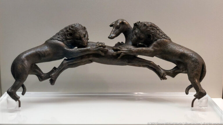 Dark bronze group of two lions reaching toward a smaller central animal across a curved support.
