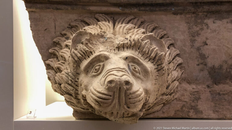 Frontal carved lion-head waterspout with open mouth and deeply radiating mane.