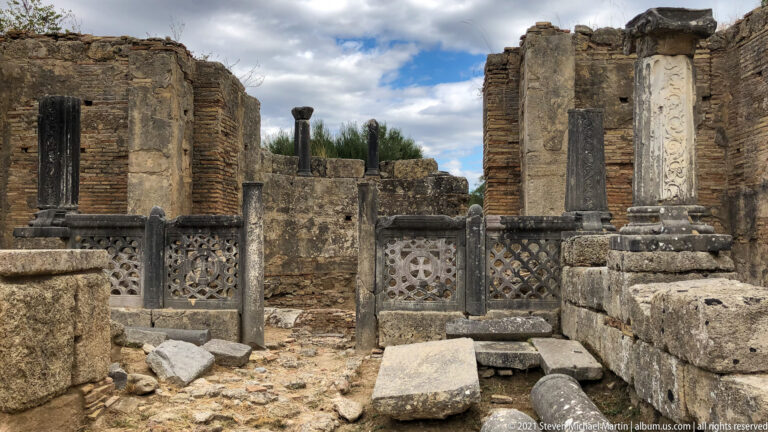 Pierced stone screen panels with circular motifs set between columns inside ancient brick and stone ruins.