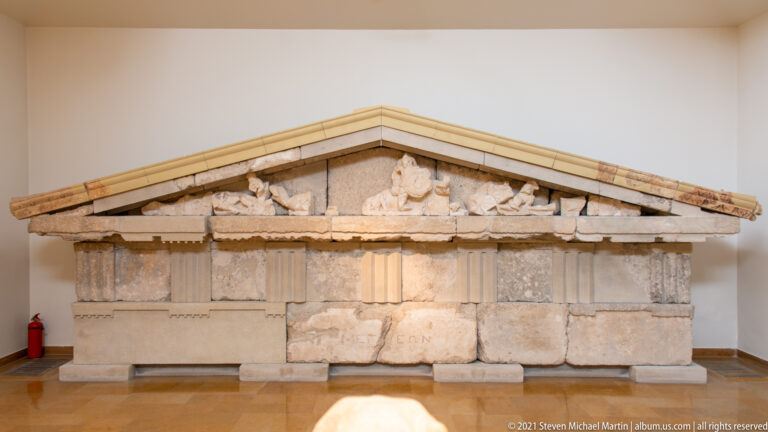 Reconstructed small Greek façade with triangular pediment, fragmentary decoration, and block-built lower wall.