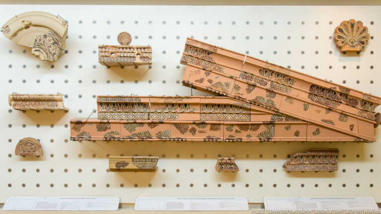 Wall display of painted terracotta architectural fragments with geometric bands, floral motifs, and palmettes.