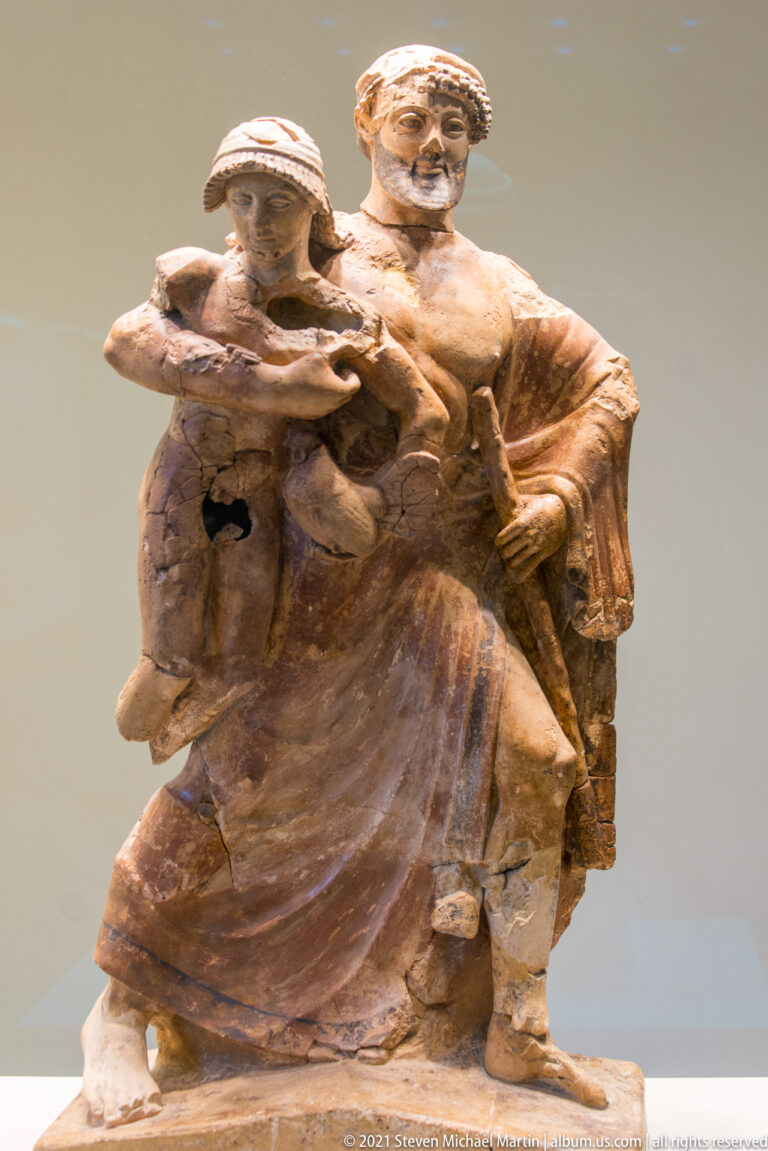 Reddish terracotta group of several clothed human figures arranged in a compact narrative scene.
