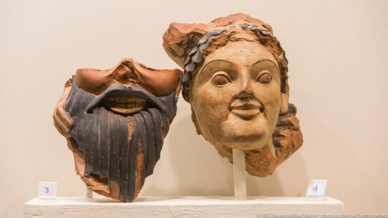 Two terracotta head fragments, one bearded with an open mouth and one smooth-faced with modeled hair.