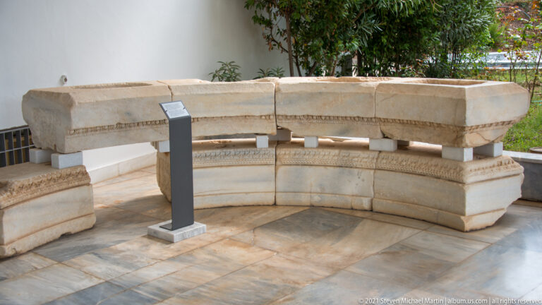 Curved museum display of pale carved architectural blocks with moldings and a central information stand.