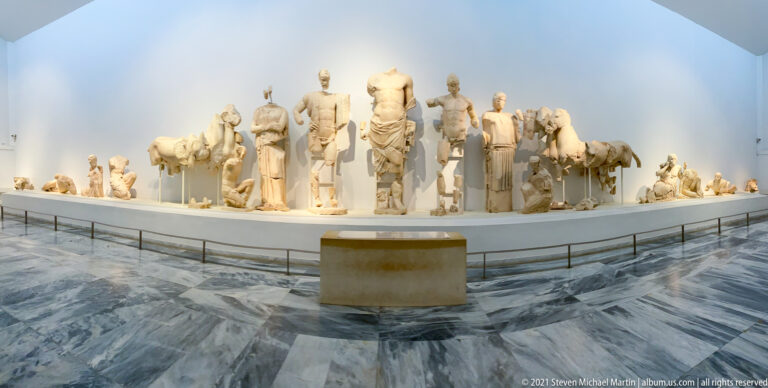 Wide museum view of monumental marble pediment sculptures from the Temple of Zeus at Olympia.