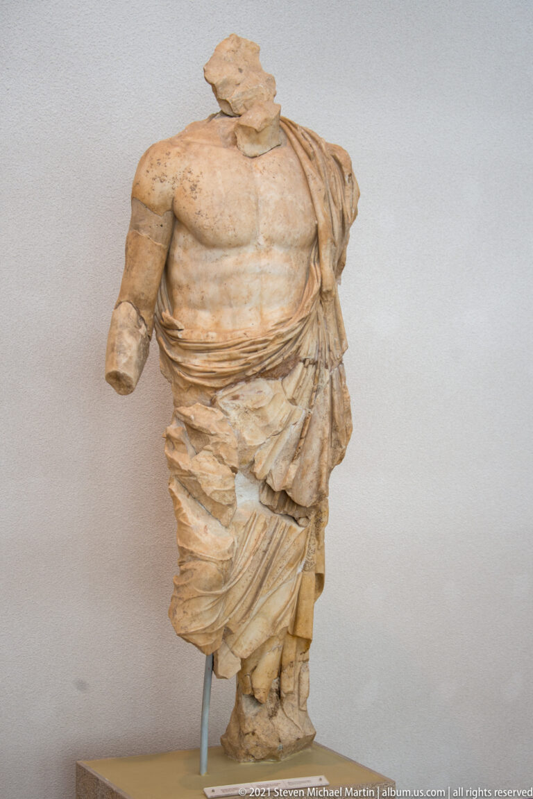 Headless muscular stone man with bare chest and a heavy mantle wrapped around his waist and legs.