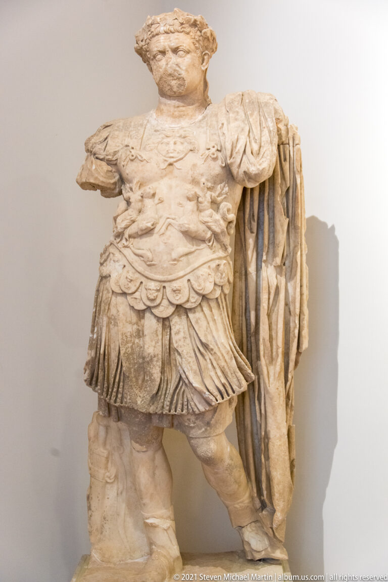 Stone male portrait statue in decorated cuirass and heavy cloak, with both arms broken away.
