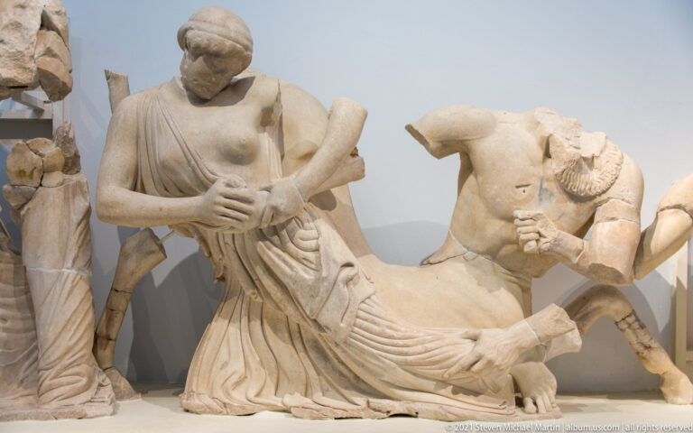 Fragmentary marble group with a kneeling draped woman beside a reclining male figure in a pedimental display.