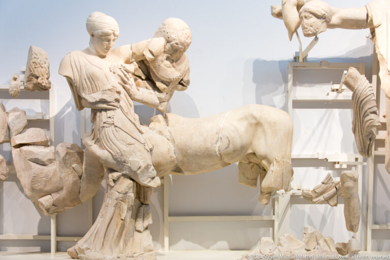 Fragmentary marble woman bending beside a centaur's horse body in the Temple of Zeus west pediment.