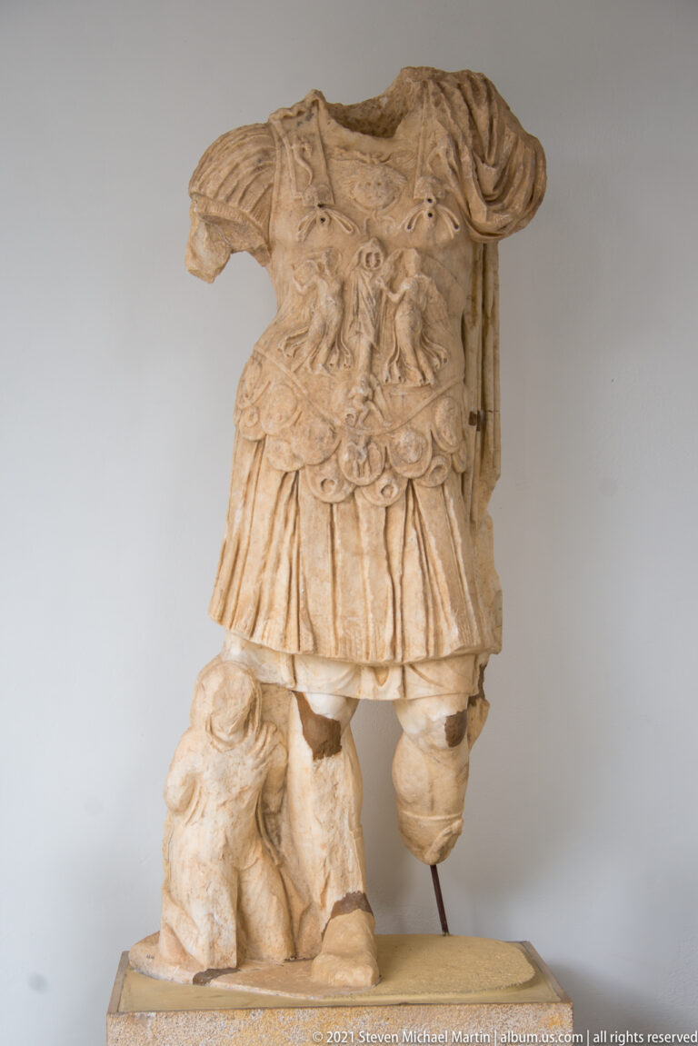 Headless marble warrior figure wearing an ornate cuirass and short pleated garment.
