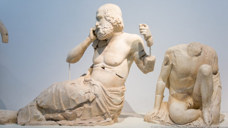 Seated bearded man and crouching nude youth in the low corner of the Temple of Zeus east pediment.