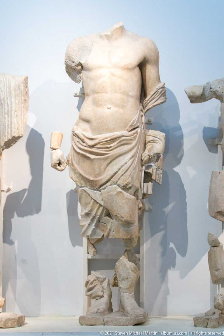 Fragmentary marble male torso with a mantle wrapped around the hips in the Temple of Zeus east pediment.