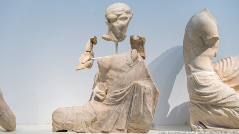 Fragmentary seated marble figure in heavy drapery with a separately mounted bearded head above the torso.