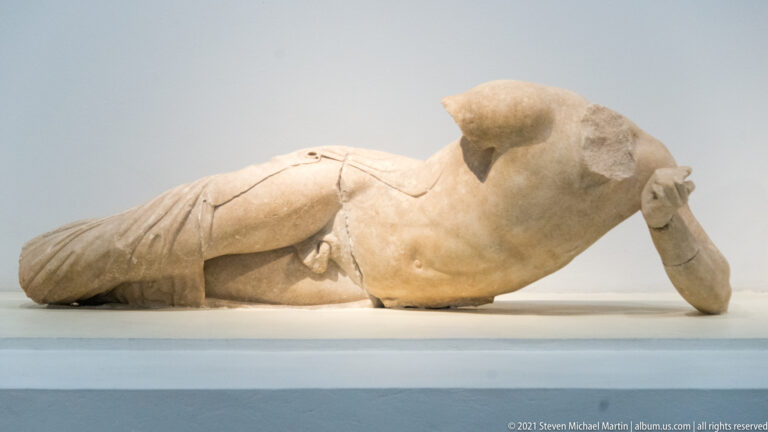 Fragmentary reclining male corner figure from the Temple of Zeus east pediment, with drapery surviving over the lower body.