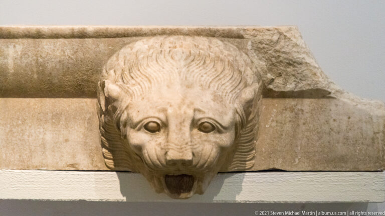 Frontal carved lion-head waterspout projecting from a rectangular architectural block.