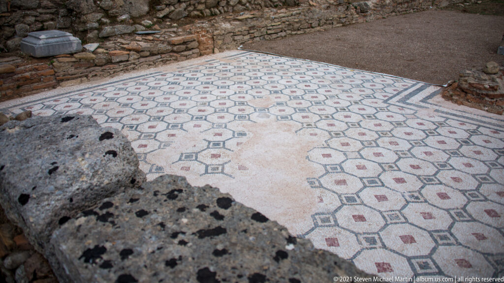 In-situ pale mosaic pavement with interlocking geometric motifs, dark borders, and small red accents.