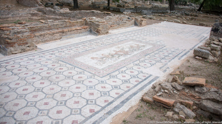 Large ancient mosaic floor with geometric patterning and a worn rectangular figural panel at the center.