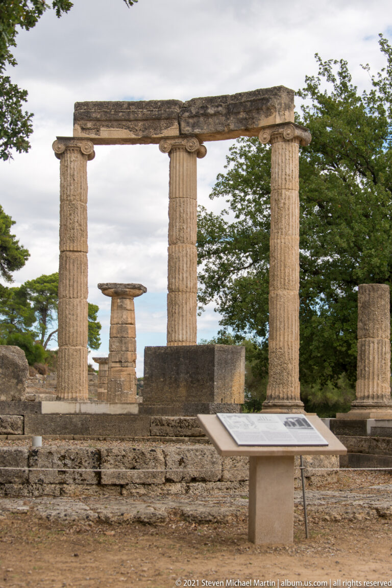 Three reconstructed Ionic columns and entablature rising from the circular foundations of the Philippeion at Ancient Olympia.