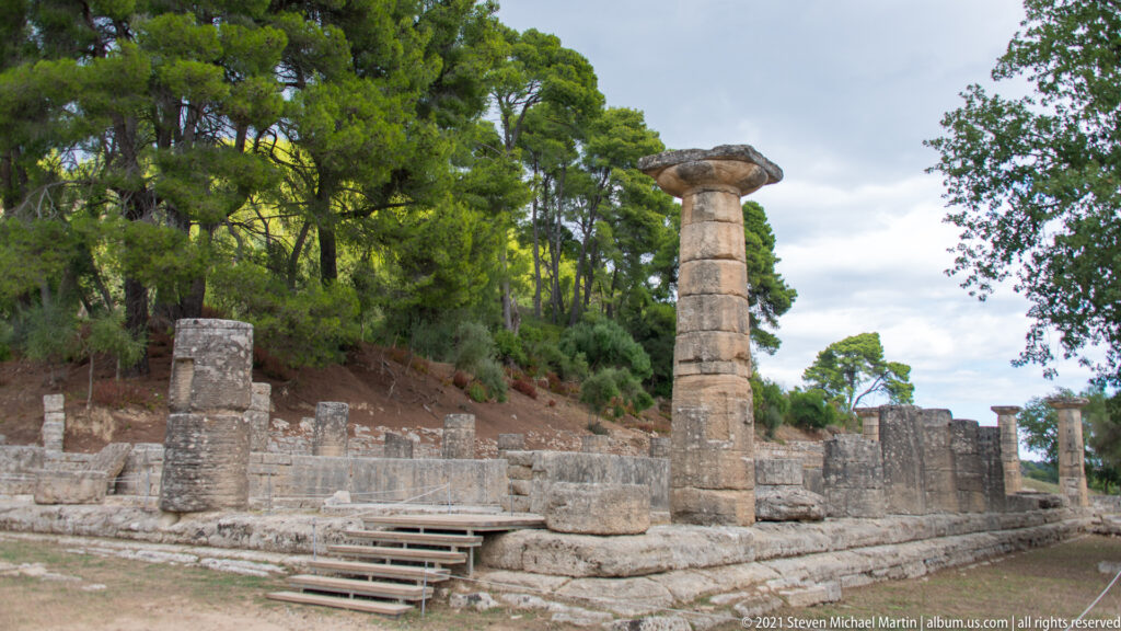 Single tall ancient column rising above low foundation walls, column stumps, and scattered blocks.