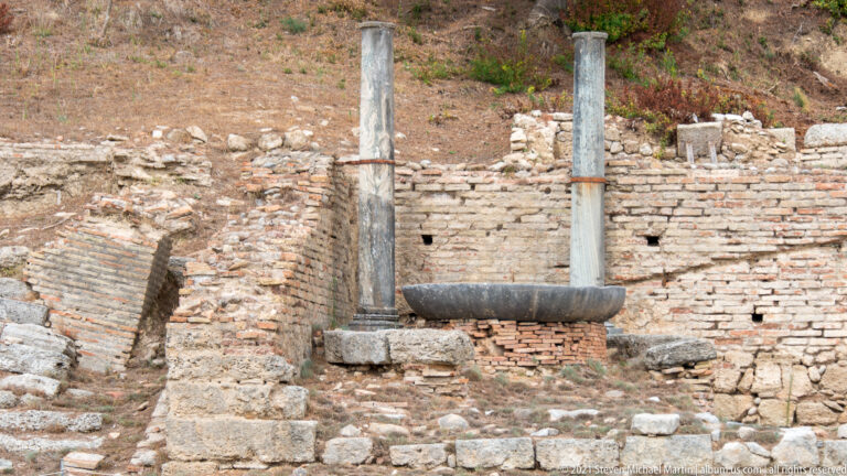 Two slender stone columns beside a curved stone basin set among brick and rubble walls.