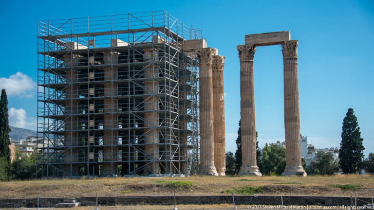 Standing Corinthian columns of the Temple of Olympian Zeus beside extensive conservation scaffolding.