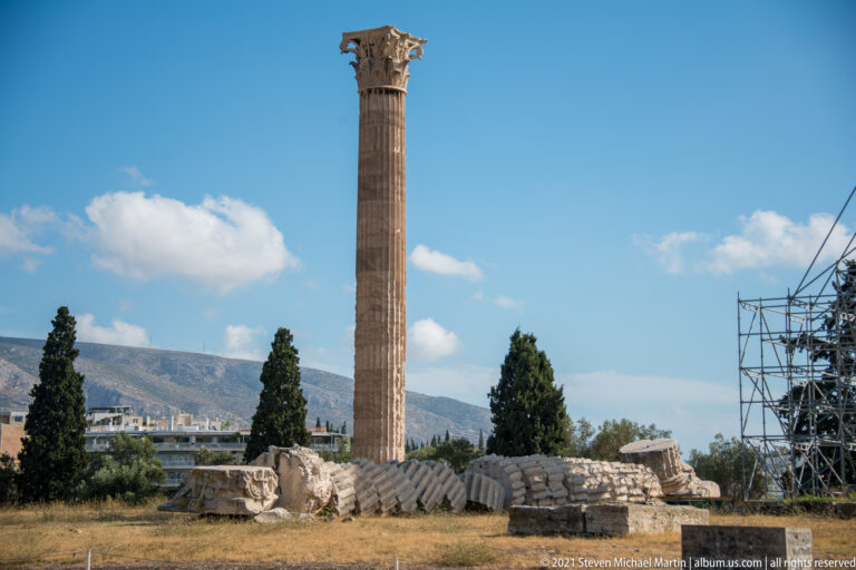 Single tall Corinthian column at the Temple of Olympian Zeus above fallen marble drums and distant mountains.