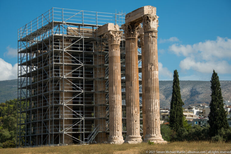 Three tall Corinthian columns of the Temple of Olympian Zeus beside dense conservation scaffolding.