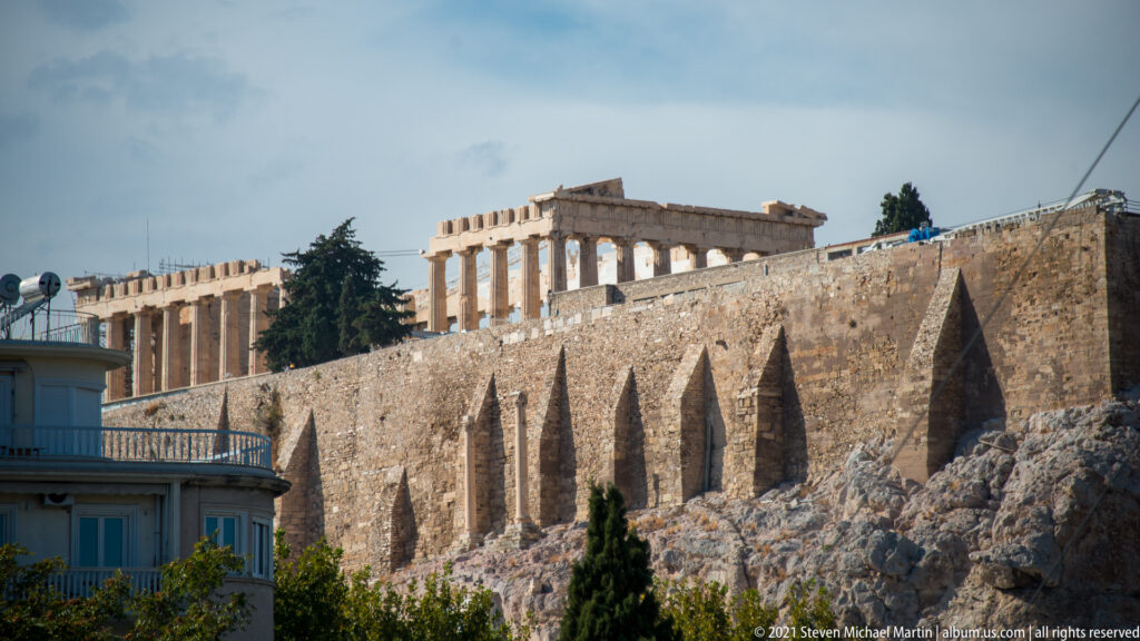 Parthenon visible above the long stone fortification wall and rocky southern slope of the Acropolis in Athens.