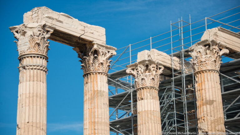Close view of Corinthian capitals and entablature fragments on Temple of Olympian Zeus columns with scaffolding behind.