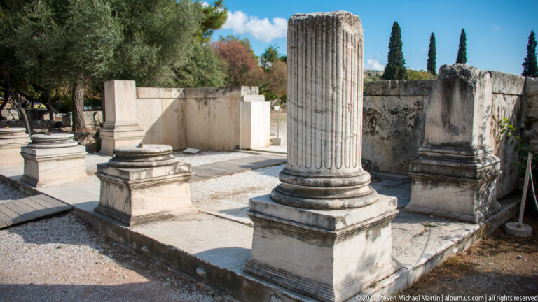 Upright fluted marble column drum with pedestal blocks and low ancient walls at the Olympieion archaeological site.
