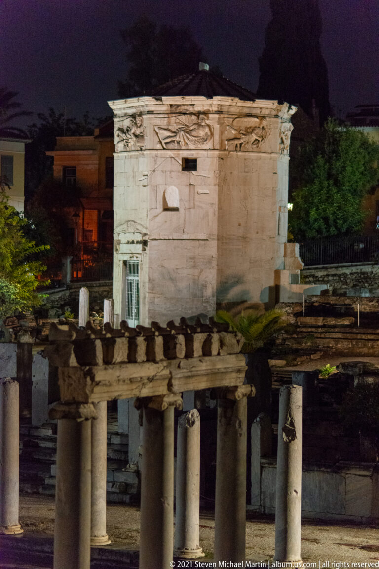 Illuminated Tower of the Winds behind a row of ancient columns in the Roman Agora of Athens at night.