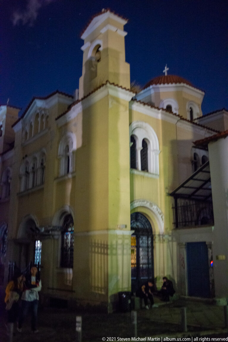Yellow-and-white Church of the Taxiarchs and the Virgin Mary Gregorousa at night, with bell tower, arched windows, and red-tiled domes.