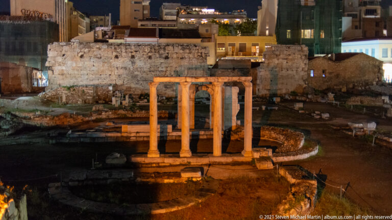 Four illuminated Ionic columns of the East Propylon in the Roman Agora, with masonry walls and excavated foundations behind.