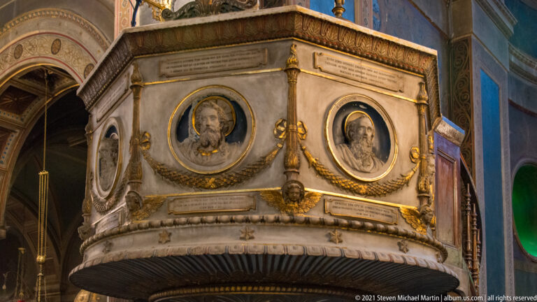 Ornate marble pulpit with portrait medallions, gilded garlands, inscriptions, and carved details inside Athens Metropolitan Cathedral.