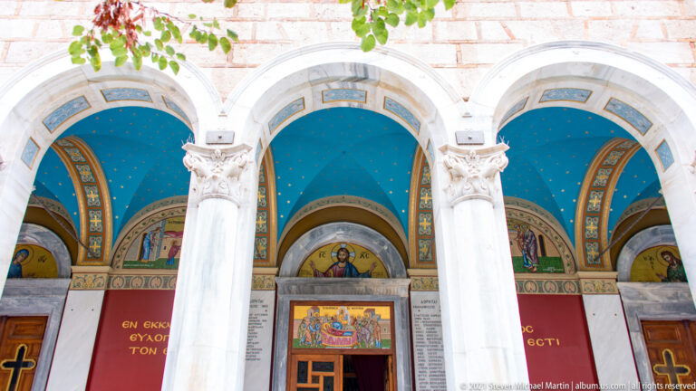 Three-arched marble portico of Panagia Chrysospiliotissa with blue starry vaults, red walls, mosaics, inscriptions, and doors.