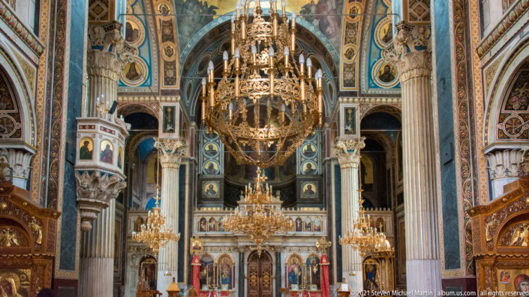 Long nave of Panagia Chrysospiliotissa with large chandeliers, painted vaults, marble columns, pulpit, icons, and sanctuary.