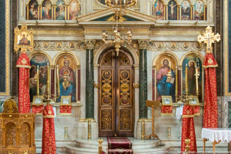 Marble sanctuary screen with gilded central doors, framed icons, red hangings, and tall candle stands.