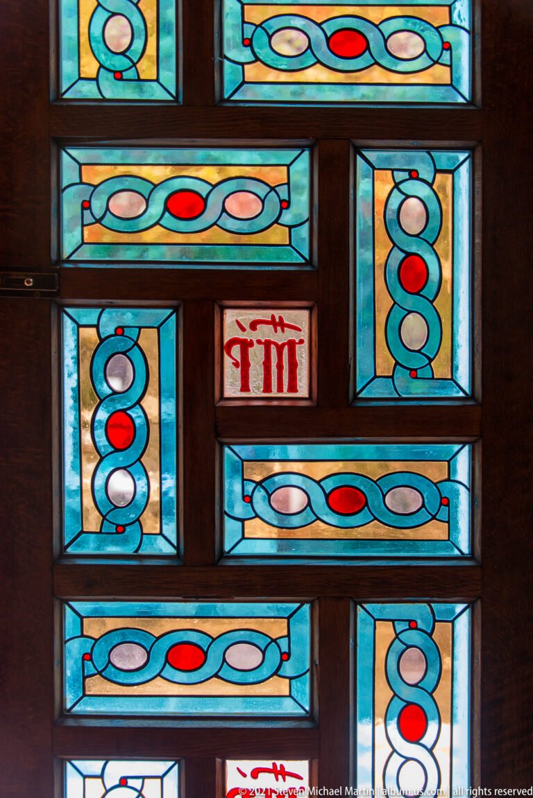 Turquoise, red, and white geometric stained-glass panels set within a dark wooden church framework.