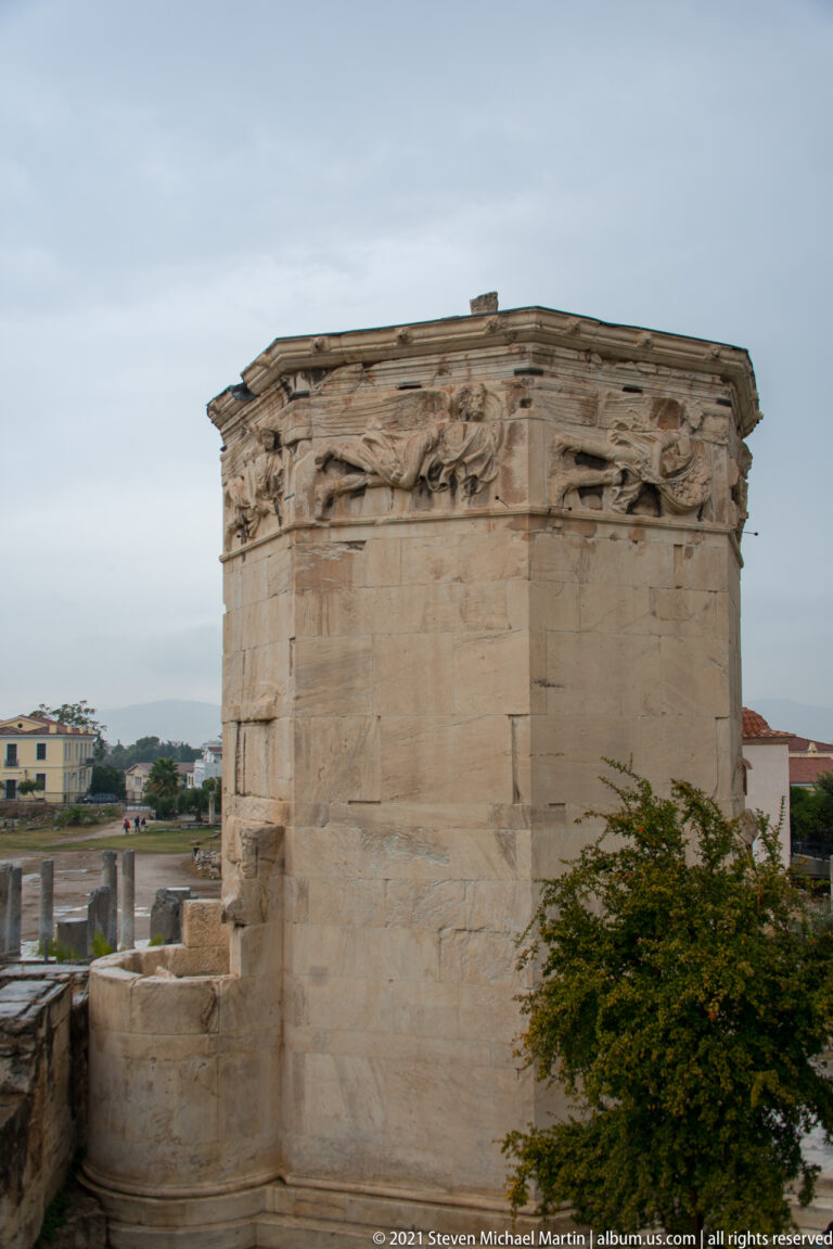 Close view of the octagonal marble Tower of the Winds with weathered relief figures along its upper walls.