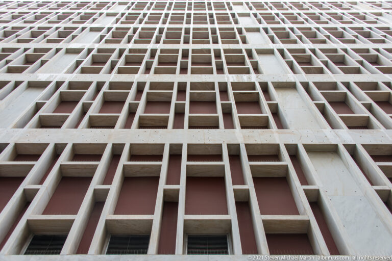 Upward view of a modern building façade formed by a deep repeating grid of rectangular concrete sunshades.