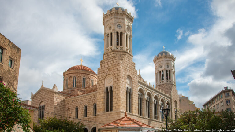 Low-angle view of the Church of Saint Irene in Athens, with twin bell towers, central dome, arched openings, and patterned masonry.