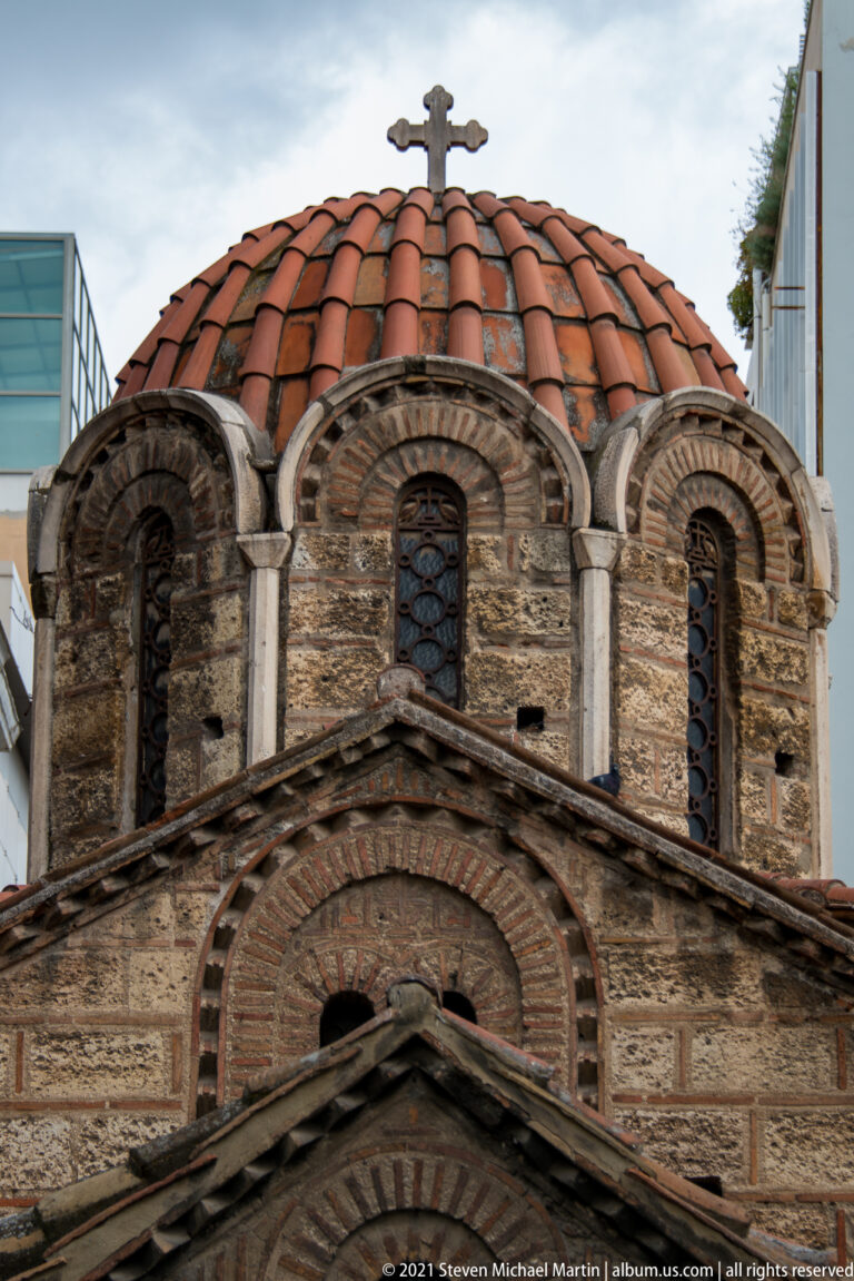 Close architectural detail of Panagia Kapnikarea with tiled dome, narrow windows, brick arches, and layered masonry.