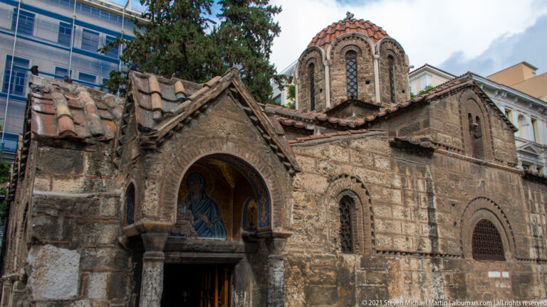 Side entrance of Panagia Kapnikarea with Virgin-and-Child mosaic, gabled tiled roof, stone walls, and arched windows.