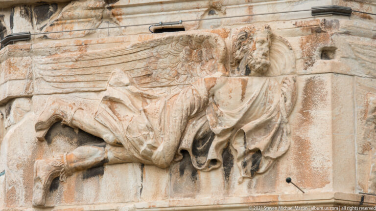 Weathered winged deity relief carved into the marble wall of the Tower of the Winds in Athens.